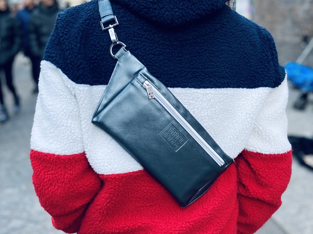 Mann in London im blau-weiß-rot gestreiften Plüsch-Hoodie, quer über dem Rücken eine Manufabo Belt Bag in Metallic-Schiefergrau